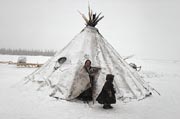 Nenets woman and boy stand by a snow covered reindeer skin tent. Yamal. Siberia
